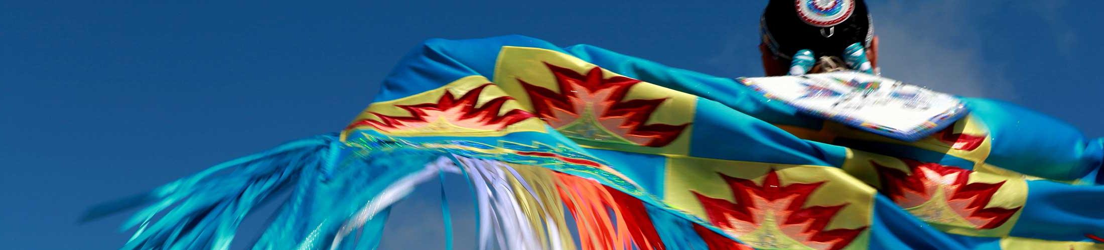 Native American in colorful native apparel with sky in background.